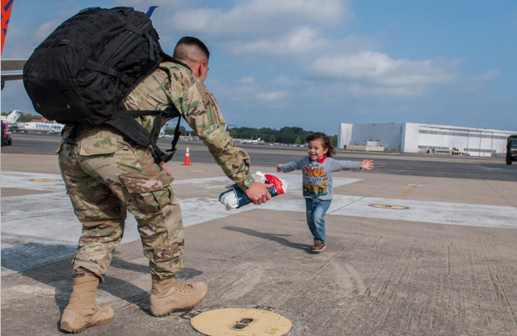 a military man bending down for a hug from a child